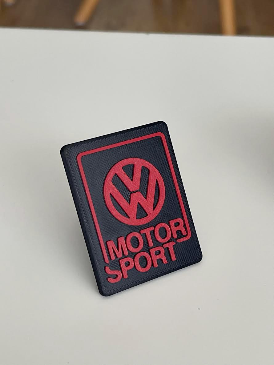 Red Volkswagen Motorsport emblem with black lettering, 3D printed for universal Volkswagen front grille installation.