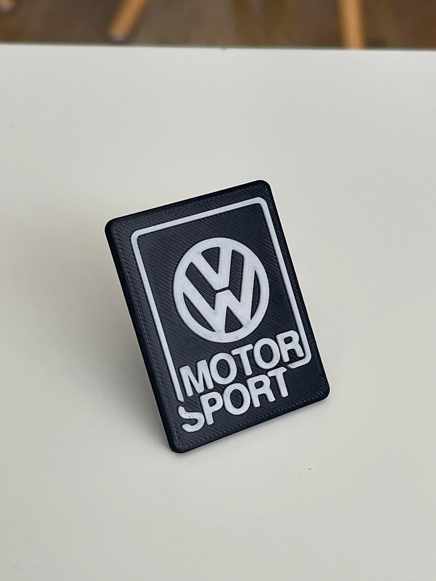 White Volkswagen Motorsport emblem with black lettering, 3D printed and designed for universal VW front grille installation.